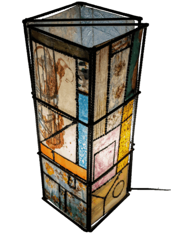 Lampada verticale a base quadrata con struttura in metallo nero, rivestita da pannelli di carta translucida colorata a collage, divisi in riquadri astratti con frammenti figurativi, campiture gialle, azzurre, rosa e segni disegnati, che diffondono la luce dall’interno.