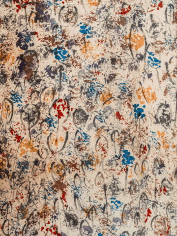 Dettaglio di un grande tessuto chiaro completamente ricoperto da impronte e segni astratti multicolori – macchie rosse, blu, gialle, viola – tra cui si riconoscono, in grigio, molte piccole vulve stilizzate ripetute come un pattern decorativo.